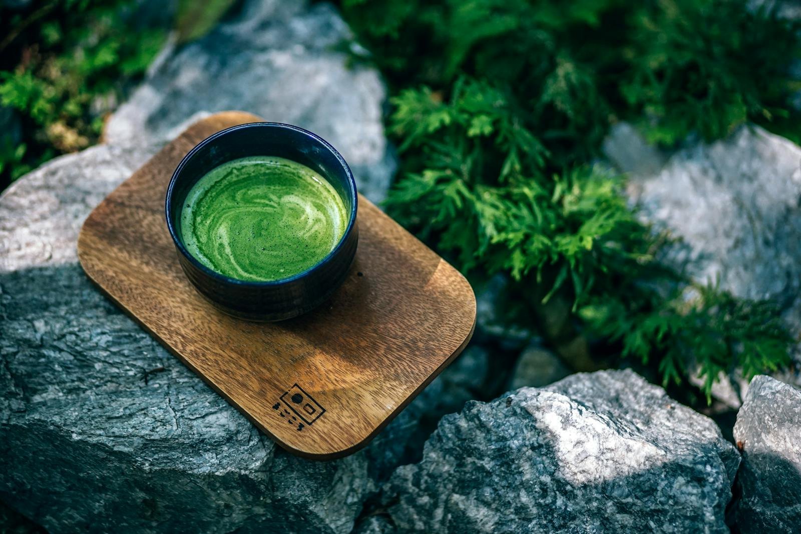 Top view of a green matcha tea served on a wooden tray outdoors, surrounded by rocks.
