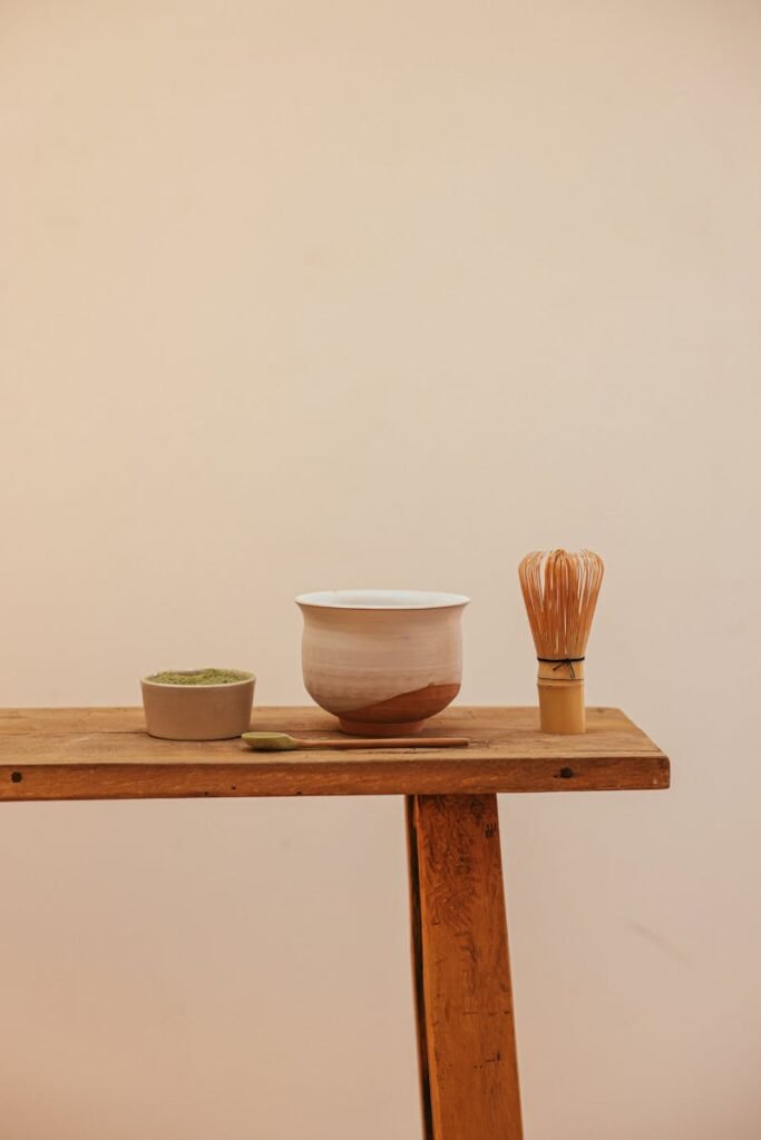 Ceremonial matcha tea accessories including a bamboo whisk and bowl on a wooden table.
