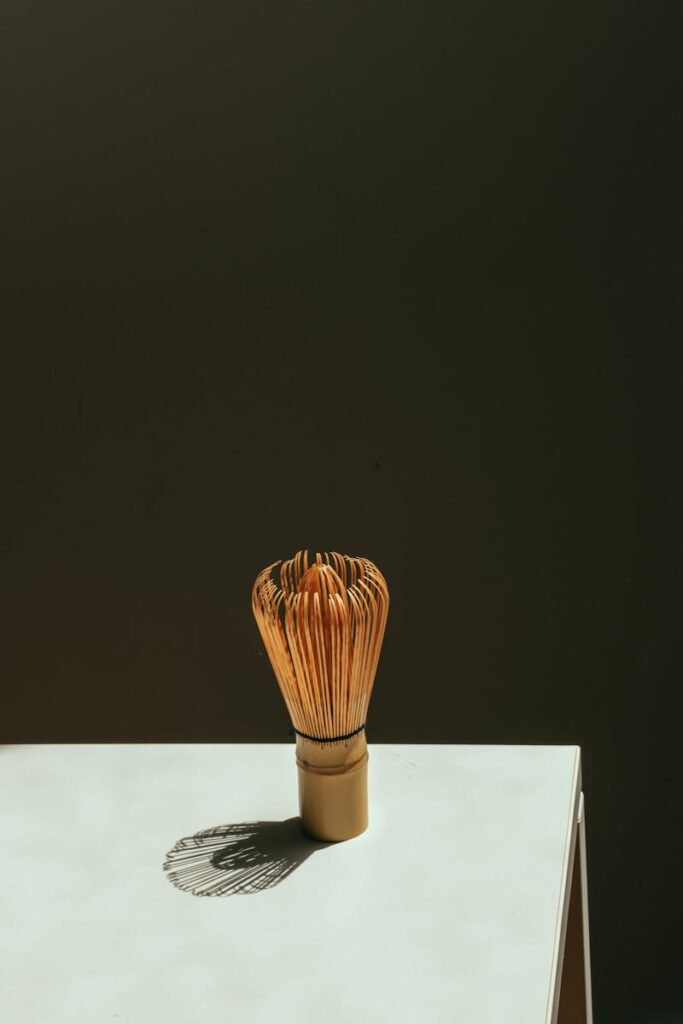 Minimalist image of a traditional matcha whisk casting a shadow on a table in studio lighting.