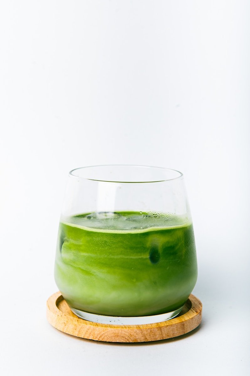 a green liquid in a glass with a wooden coaster